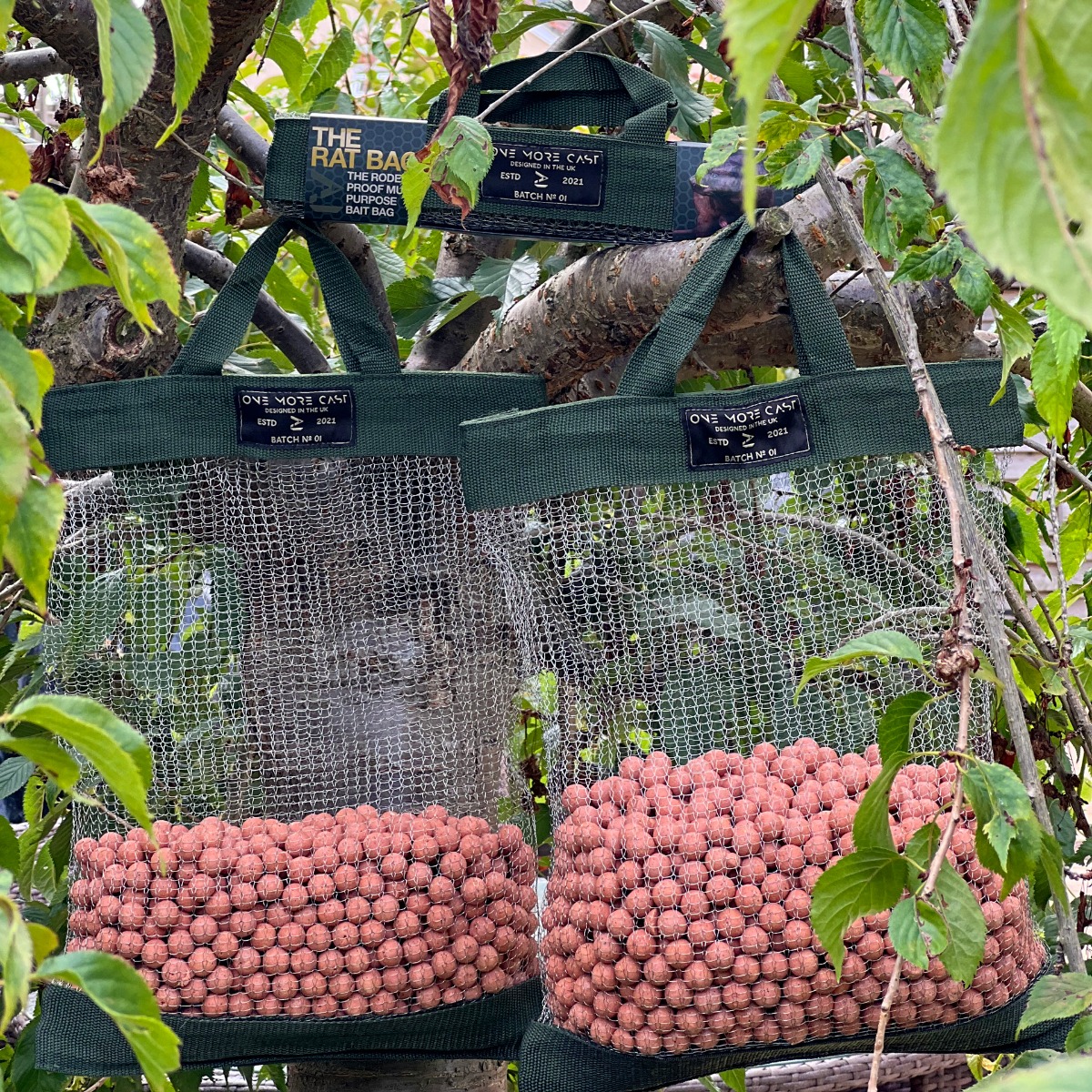 Two One More Cast rat bags hanging in tree, with boilies in bag