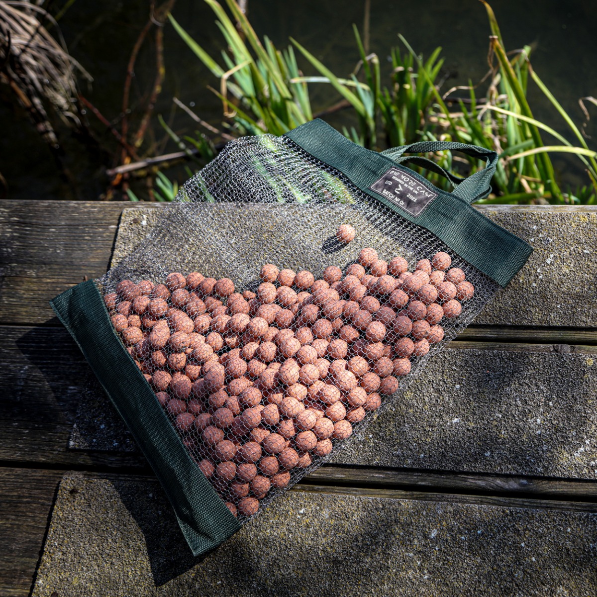 One More Cast rat bag laying on wooden stage, with boilies in bag